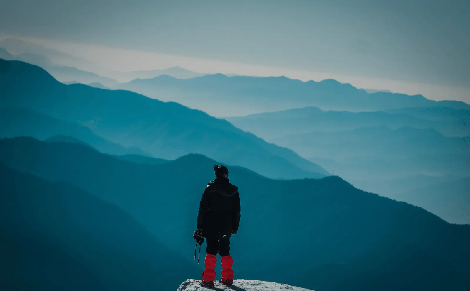 Boy standing triumphantly on a mountain peak, enjoying panoramic Himalayan views.